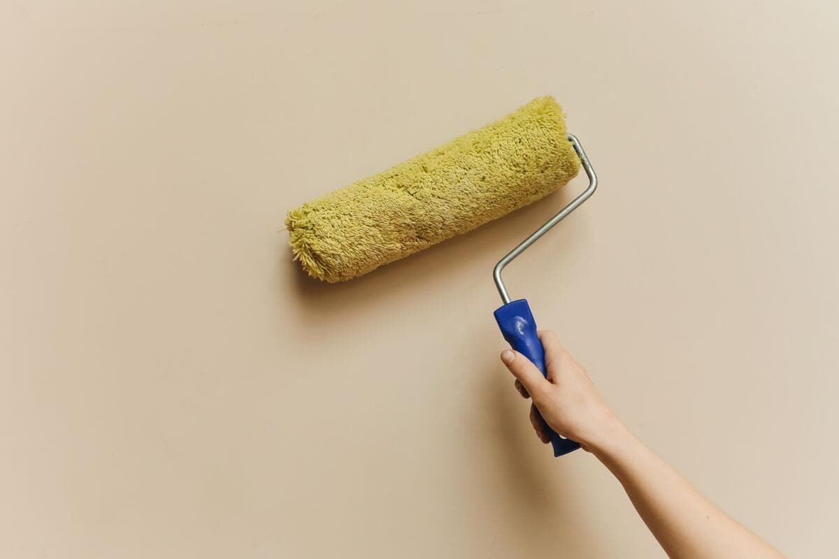 O que o orçamento de pintura deve detalhar Rolo amarelo pintando parede bege durante reforma residencial