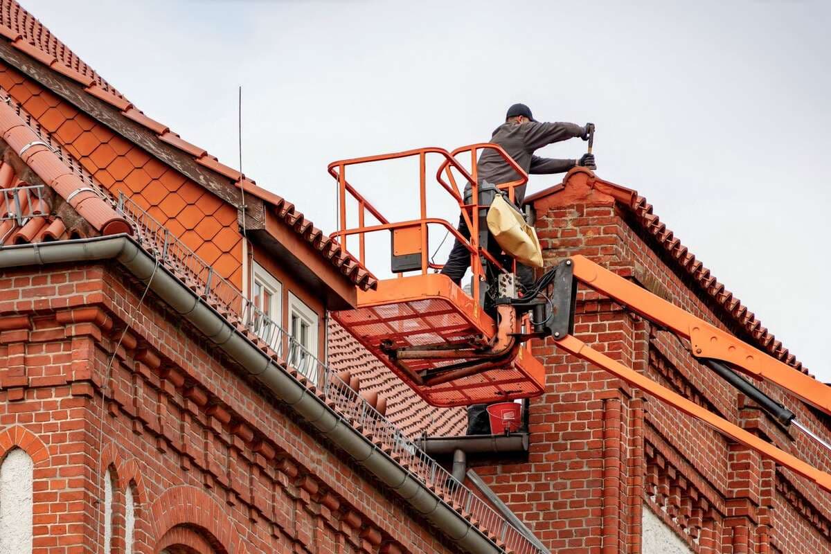 Profissional em plataforma elevatória fazendo manutenção em telhado de telhas cerâmicas