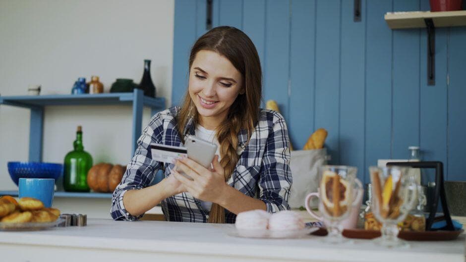 Mulher sorrindo enquanto faz um pagamento pelo celular com cartão na mão