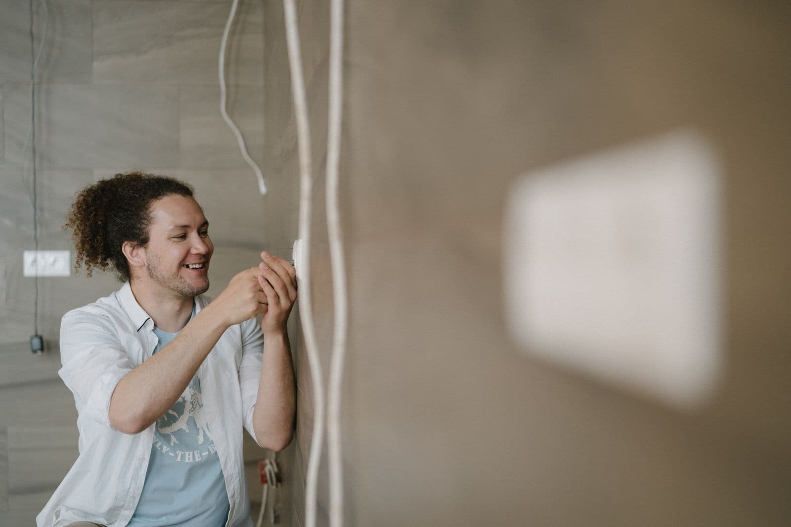 Eletricista sorrindo enquanto instala uma tomada na parede de uma residência.