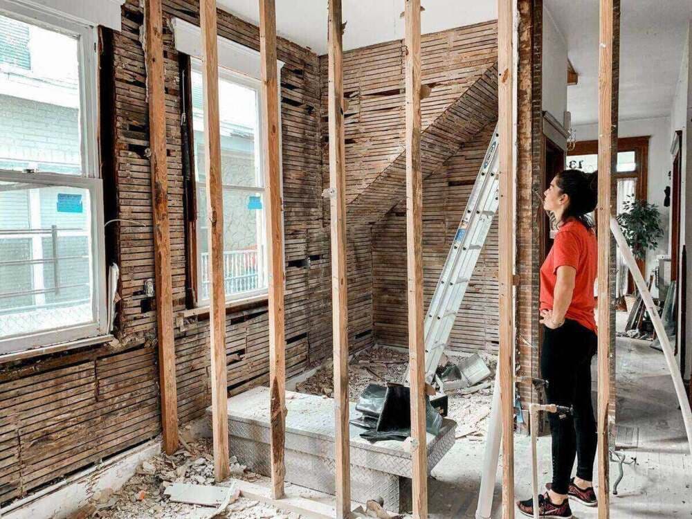 Mulher em cômodo com reforma em andamento, avaliando o acabamento antes da entrega